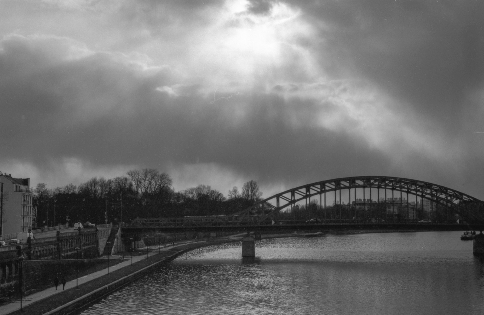 Łukowy stalowy most nad rzeką pod ciężkimi, dramatycznymi chmurami