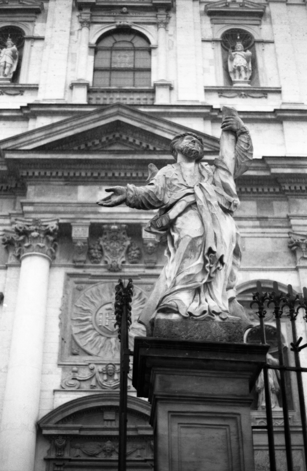 Kamienna rzeźba apostoła z wyciągniętą ręką na tle fasady kościoła