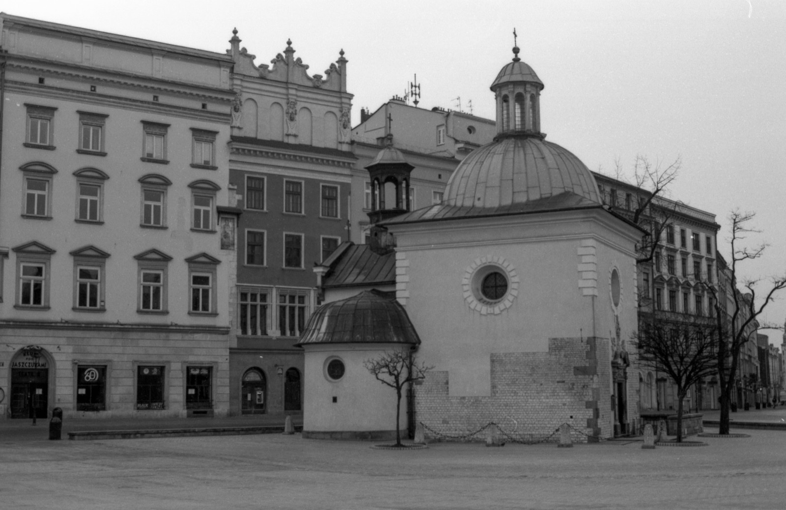 Mały kościół z kopułą i okrągłym oknem na tle kamienic, przed nim bezlistne drzewa